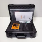 An open black aluminum hard case with protective foam padding containing the orange Temtop PMD351 particle counter, an accessory pouch, and the official user manual document.